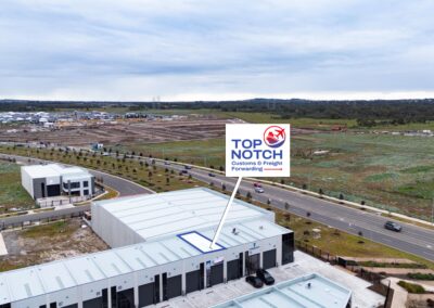 DJI_20260806155641_0012_D - Top Notch Customs Aerial view of a developing industrial park with rows of warehouses and roads, and a prominent sign reading 'Top Notch Customs & Freight Forwarding' in the foreground.